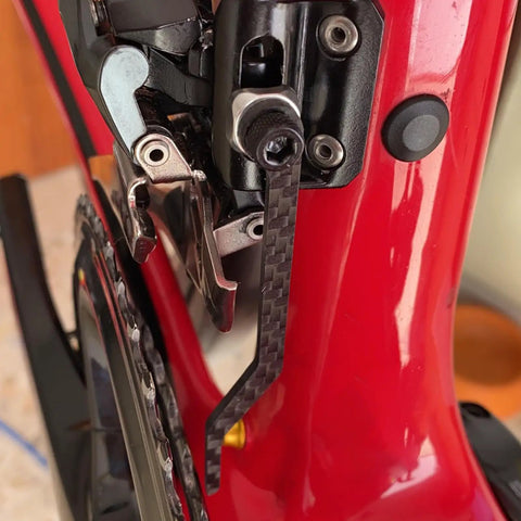 Close-up of Tough As Nails Carbon Fiber Chain Catcher For Road Bikes, mounted on red bike frame, securing chain near front derailleur.