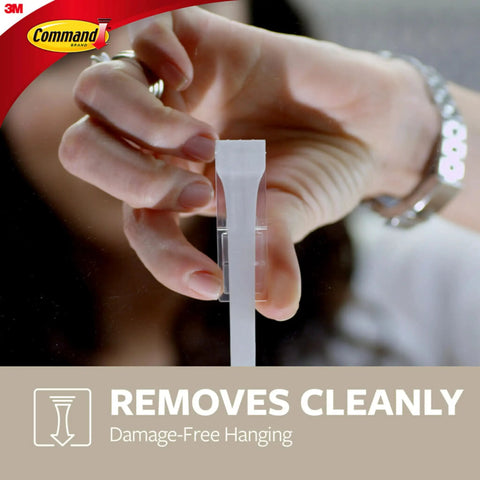 Close-up of person peeling Command strip showcasing Large Designer Hook Holds Up To Five Pounds With Two Strips Brushed Nickel Finish Damage Free Wall Hook No Tools Needed For Quick Decor Hanging And Everyday Organization In Living Spaces.