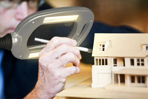 Person using MultiFlex LED Floor Magnifier Lamp with wide 6-inch viewing area for crafting, showing silver finish and bright LED lighting.
