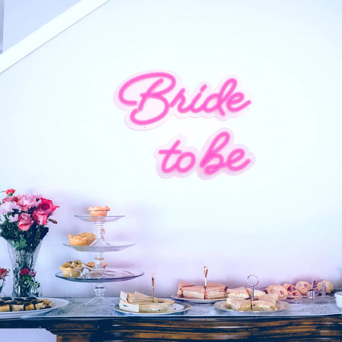Bride to Be Neon Sign for Weddings and Bachelorette Parties, 17x13 Inch LED Light Up Decor above dining table with snacks.