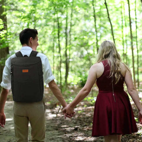 Couple walking through forest, man carrying Soft Backpack Cooler For 30 Cans, Insulated Leakproof Travel Lunch Tote on back.