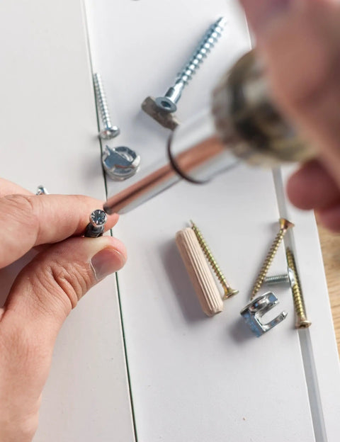 Person using a screwdriver on M6 X 40mm zinc cam lock screws, with various hardware parts visible for furniture assembly.