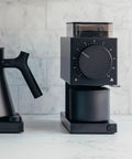 64mm Flat Burr Electric Coffee Grinder Built For Brewed Coffee Lovers With 31 Grind Settings next to pour-over kettle on counter.