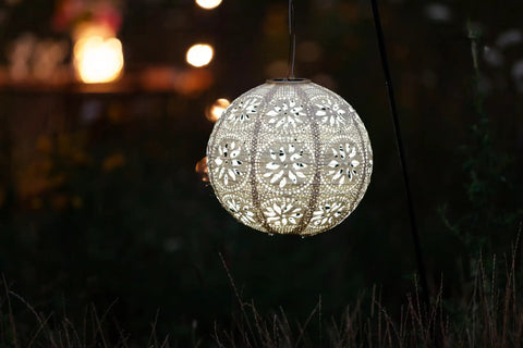 LED Outdoor Solar Lantern For Patio And Deck Handmade Tyvek Weather Resistant UV Rated Stainless Steel Hardware Auto Sensor On Off Energy Efficient Garden Light That Is Lit In Pearl, glowing at night in garden setting.
