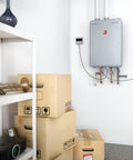 Skip The Clunky Tank For This High Efficiency Natural Gas Tankless Water Heater Delivering Straight Fire Whole Home Hot Water At 9.5 GPM With Smart Leak Alerts And Ultra Compact Footprint mounted in a storage area with boxes.