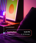 E12 Candle Color Wi Fi Smart LED Light Bulb With Polychrome Technology illuminating beside a framed artwork in a bedroom setup.