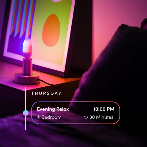 E12 Candle Color Wi Fi Smart LED Light Bulb With Polychrome Technology illuminating beside a framed artwork in a bedroom setup.