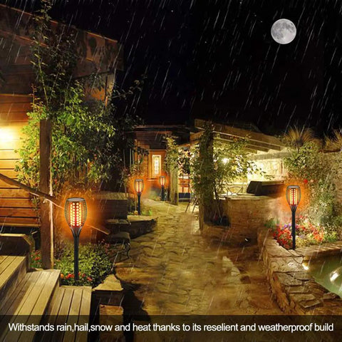 43 Inch Solar Torch Lights With Realistic Flickering Flames 2 Pack illuminating a rainy backyard path at night
