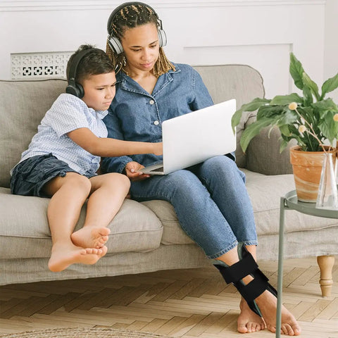 Woman sitting on couch with Air Gel Ankle Brace with Stirrup Support for Upright Stability and Quick Relief, using a laptop