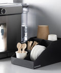 Coffee Station Organizer With 4 Compartments Perfect For Storing Coffee Pods Sugar Creamer Stirrers And Tea Bags On Your Office Or Kitchen Countertop For Quick Grab And Go Access And Neat Countertop Organization positioned next to coffee machine on counter.