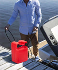 Person carrying Six Gallon Portable Marine Fuel Tank For Outboard Boats With 9.8 Ft Hose And Built In Level Gauge by a boat dock.