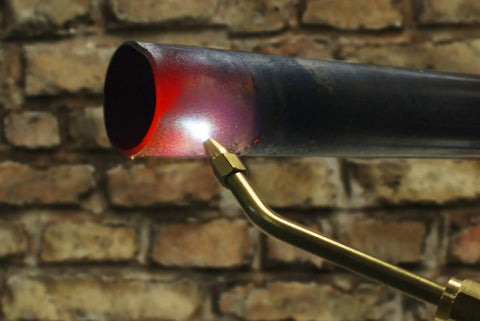 Oxypropane Welding Gas Cutting Torch Kit with brass fittings in use, heating metal pipe against brick wall backdrop.
