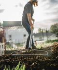 A person using a Powerful Workhorse Metal Bow Rake With Heavy Duty Steel Construction And No Slip H Grip Ergonomic Handle for gardening.