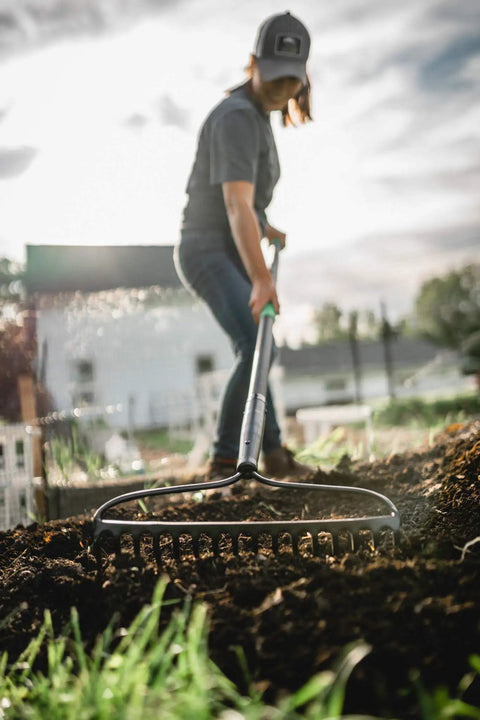 A person using a Powerful Workhorse Metal Bow Rake With Heavy Duty Steel Construction And No Slip H Grip Ergonomic Handle for gardening.