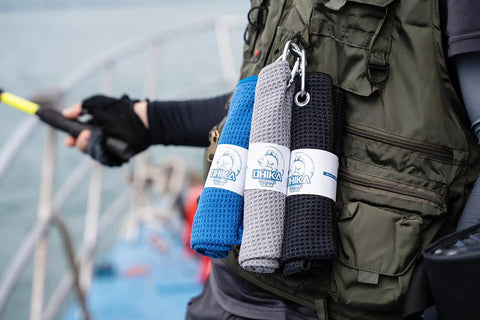 Grab And Go Clip On Microfiber Fishing Towels With Waffle Pattern in blue, grey, and black clipped to a green fishing vest.