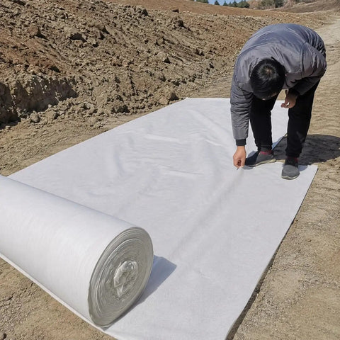 Person unrolling a Heavy Duty Polyester Ground Cover Mat With Built Like A Tank Weed Barrier and Water Permeable Drainage Design.