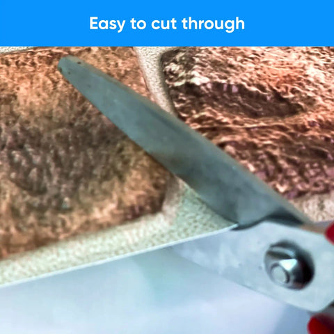 Close-up of cutting 3D Faux Stone Wall Panels Non Adhesive PVC Covering 50 Sq Ft For Home And Office Decor, 10 Pack with scissors.