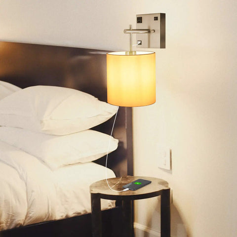 Bedside Wall Sconce With USB Port And AC Outlet, White Fabric Shade, Hardwired Mount Light, shown in bedroom setup, bulb lit