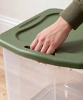 Hand gripping the lid of the Rock Solid 95 Quart Clear Plastic Storage Bin With Easy Grip Handles for organization.