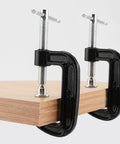 Fifteen Piece 2 Inch G Clamp Set Black Metal C Clamps With 50mm Jaw Opening For Woodworking Metalworking And Assembly Projects Great For Welding And Fastening Heavy Duty Cast Iron Frame Delivers Strong Grip And Smooth Clamping. Two black 2-inch cast iron C clamps holding a wooden board