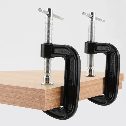 Fifteen Piece 2 Inch G Clamp Set Black Metal C Clamps With 50mm Jaw Opening For Woodworking Metalworking And Assembly Projects Great For Welding And Fastening Heavy Duty Cast Iron Frame Delivers Strong Grip And Smooth Clamping. Two black 2-inch cast iron C clamps holding a wooden board