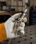 Ultimate TIG Wire Feeder Tool With Magnetic Base And Heat Shield For Alloy Filler Rods, hand-held in glove during metalwork.