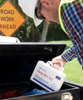 First Aid Kit (91324), white; loaded into a truck bed by a worker in a hard hat; road work ahead sign in background.