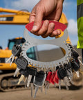 Hand holding Heavy Equipment Master Pro Grade Key Set For Construction Machinery With 43 Keys For 21 Major Brands in front of excavator.