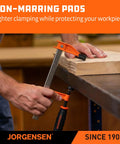 Two Jorgensen steel bar clamps (orange/black) securing wood on a workbench.