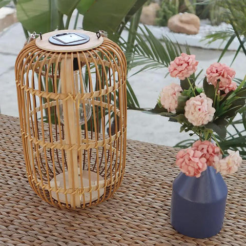 Large Outdoor Solar Lantern With Rattan And Bamboo Build Dope Glow For Garden Patio And Yard Waterproof Hanging Lantern With Handle And Edison Bulb Openwork Design For Tabletop Decoration on woven table next to flowers.