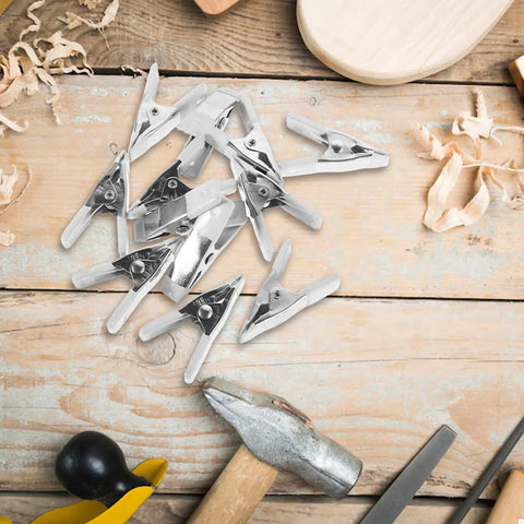 Super Heavy Duty 12-Pc Metal Spring Clamps Kit With Tough White Tips Perfect For Woodworking, DIY Panels, And Backdrop Stands To Hold Projects Steady In Home Shop Or Studio Setting, 12-piece metal clamps on wood table