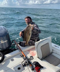 Man holding a large fish on a boat with fishing gear in the ocean