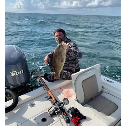 Man holding a large fish on a boat with fishing gear in the ocean