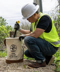 Worker using 12 Inch Canvas Utility Bucket With Leather Bottom And Reinforced Leather Rim Natural Color With Multicolor Trim One Inner Pocket Heavy Duty American Made Work Tote For Tools Klein Tools Style outdoors.