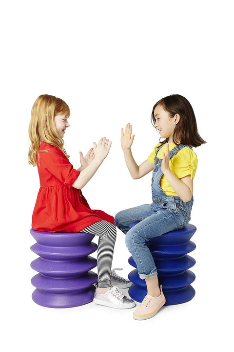 Two kids playing patty-cake on purple stools. Active Sitting Stool for Kids Ergonomic Wiggle Friendly Desk Chair Designed to Boost Focus