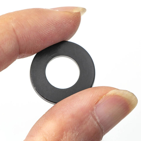 Close-up of a single black washer from Do It All Nylon Washer Kit 720 Pieces Assortment From M2 To M12 Flat Washers For Bolts And Screws PA66 Nylon Insulation Friendly 9 Sizes Durable Hardware Set For Mechanical And Electrical Jobs held between fingers.