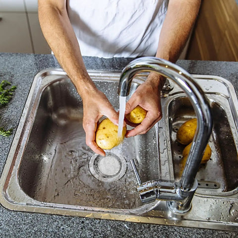 Person washing potatoes over a sink with 2 Pack Stainless Steel Kitchen Sink Strainer Set With Wide 4.5 Inch Rim Fits Most Standard Drains And Garbage Disposals Rust Free With 2mm Holes Smooth Rolled Rim That Will Not Scratch Hands installed in the drain