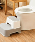 Two Step Toddler Stool Set Of Two, Super Sturdy Non Slip Bath Footrest For Kids Potty Training And Sink Washing, Straight Up Essential For Growing Toddlers, Wide Grip Platform, Light Grey placed near a toilet.