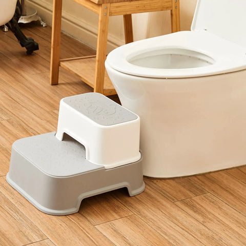 Two Step Toddler Stool Set Of Two, Super Sturdy Non Slip Bath Footrest For Kids Potty Training And Sink Washing, Straight Up Essential For Growing Toddlers, Wide Grip Platform, Light Grey placed near a toilet.