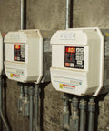 Three industrial electrical panels mounted on a concrete wall, featuring digital displays and high voltage warning signs.