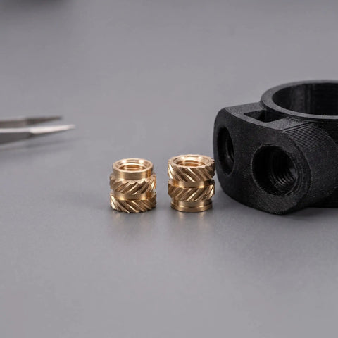 Premium 48Pcs Brass M4 Heat Set Threaded Inserts For 3D Printing With Knurled Design next to a 3D printed black part.