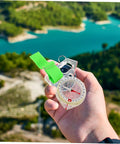 Thumb Type Directional Compass For Outdoor Navigation, Portable Hiking Tool held in hand overlooking a lake