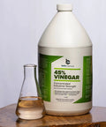 Industrial Strength 45 Percent Pure Vinegar Concentrate For Heavy Duty Cleaning And Degreasing, 1 Gallon Bottle next to glass container