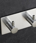 Heavy Duty Stainless Steel Wall Mounted Hooks Featuring Super Strong Self Adhesive Tape For Bathroom Towels Coats And Home Organization No Drill Hassle Rust Proof Daily Setup mounted on a dark wall.