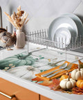 Sage Green Pumpkin Dish Drying Mat For Kitchen Counter Absorbent Microfiber Surface With Wood Grain Leaves Autumn Decor 16 By 18 Inches Machine Washable shown on kitchen counter with dishes, display of autumn decor and turkey figurine.