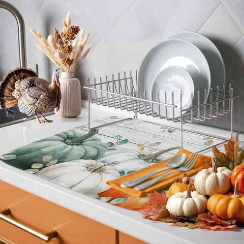 Sage Green Pumpkin Dish Drying Mat For Kitchen Counter Absorbent Microfiber Surface With Wood Grain Leaves Autumn Decor 16 By 18 Inches Machine Washable shown on kitchen counter with dishes, display of autumn decor and turkey figurine.
