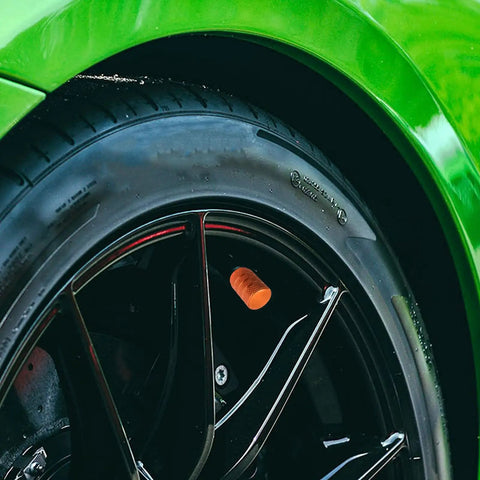 Close-up of a tire with 5 Piece Aluminum Tire Valve Stem Cap Set in orange anodized finish on a car wheel.