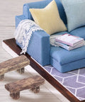 4 Pack Miniature Resin Park Benches for Fairy Gardens and Dollhouses placed near a blue fabric sofa with pillows and books