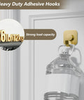Heavy Duty Adhesive Wall Hooks In A Dope Four Pack, Stainless Steel Stick On Hangers With Badass Grip For Bathrooms And Kitchens, Waterproof And Super Fast To Put Up On Any Wall Or Door Without Drilling, Classic Gold Finish holds a water jug on a door.