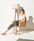 Tall Tripod Floor Lamp With Wood Legs And Cream Drum Shade next to seated woman, showcasing modern mid-century style in living room.